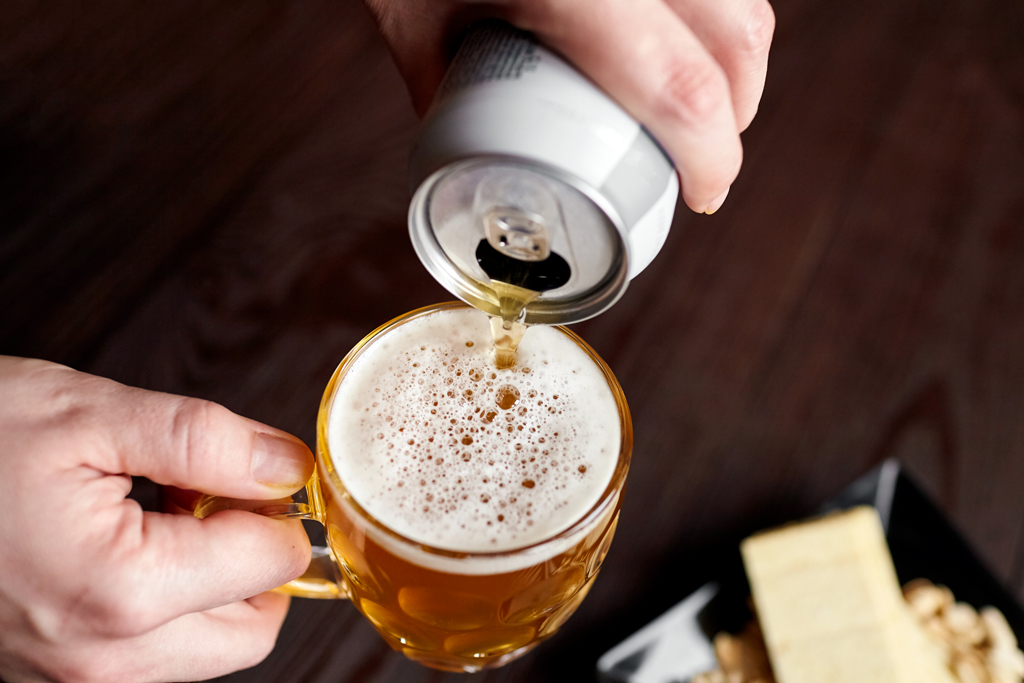 Gross plan sur une main versant une canette de bière dans un verre
